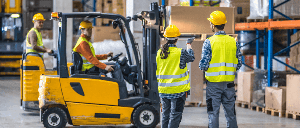 A group of employees working in a warehouse, safely operating forklifts.