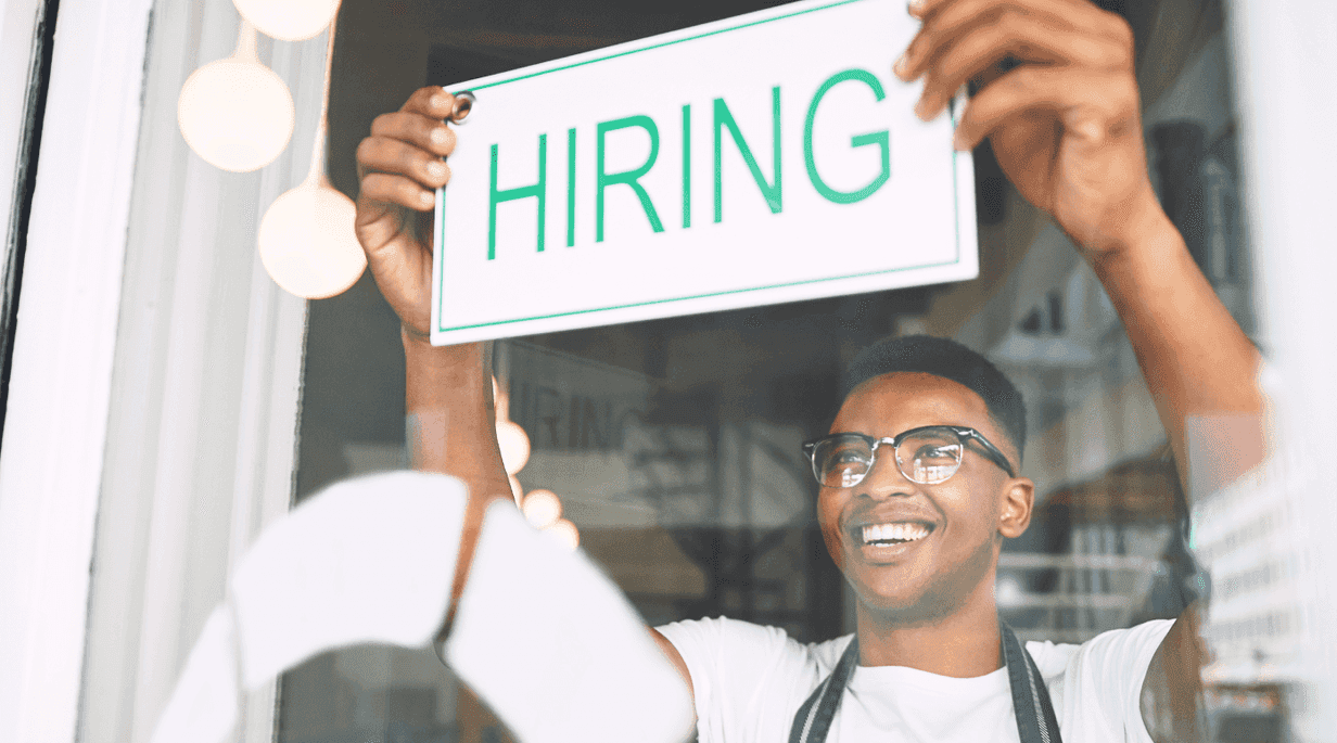 Young man placing hiring sign in window of retail store