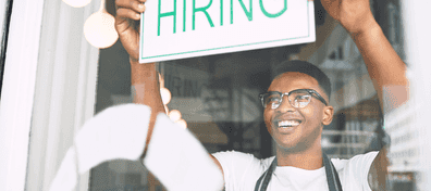 Young man placing hiring sign in window of retail store