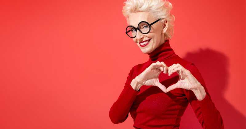 Older woman with short gray hair and red sweater making a heart shape with hands