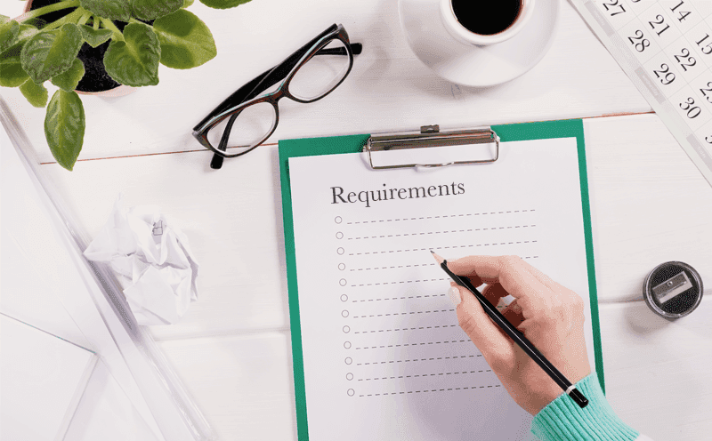 Person using a pen to write a list of requirements on paper