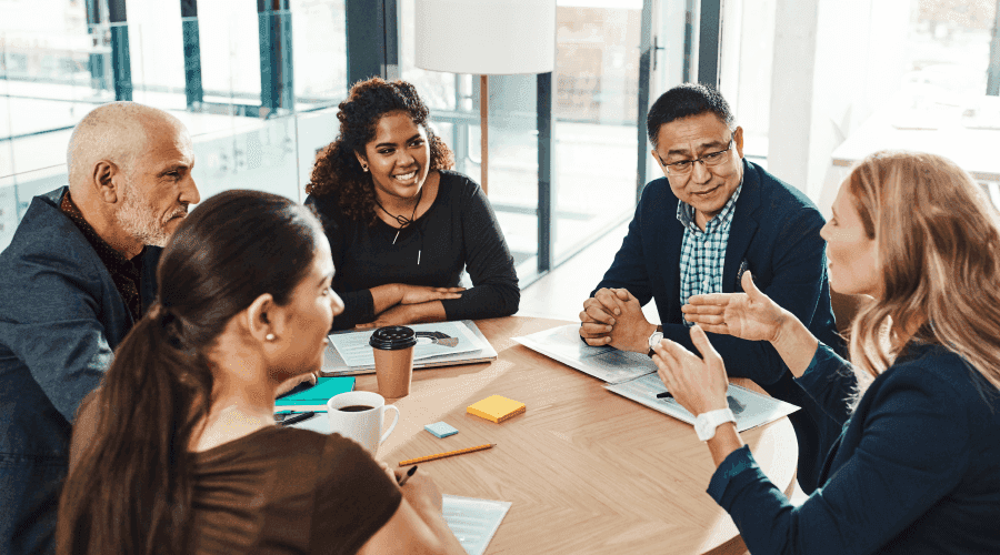 A group of employees from different age groups are working together around a conference room table.