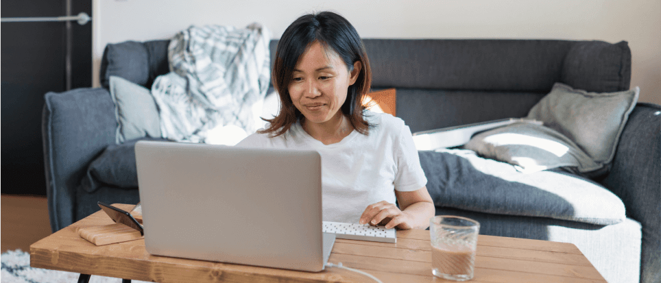 An Asian-American woman works at home on her laptop in the living room.