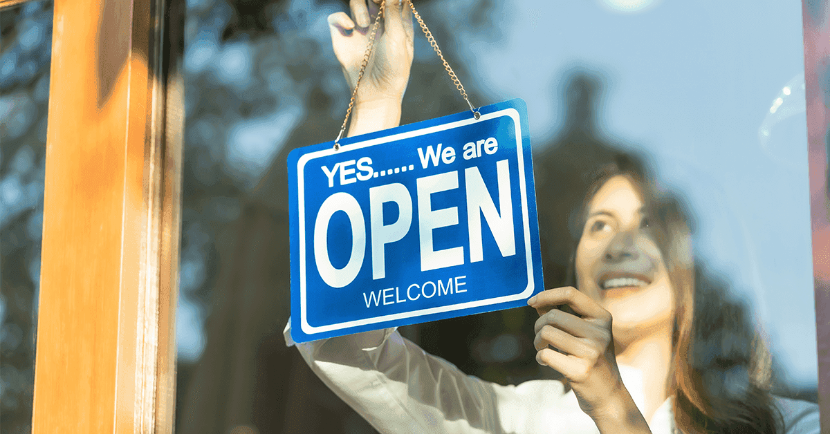 Woman hanging an Open sign in shop window